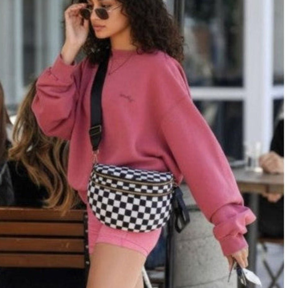 Person wearing a pink sweatshirt and checkered shorts walking outdoors.
