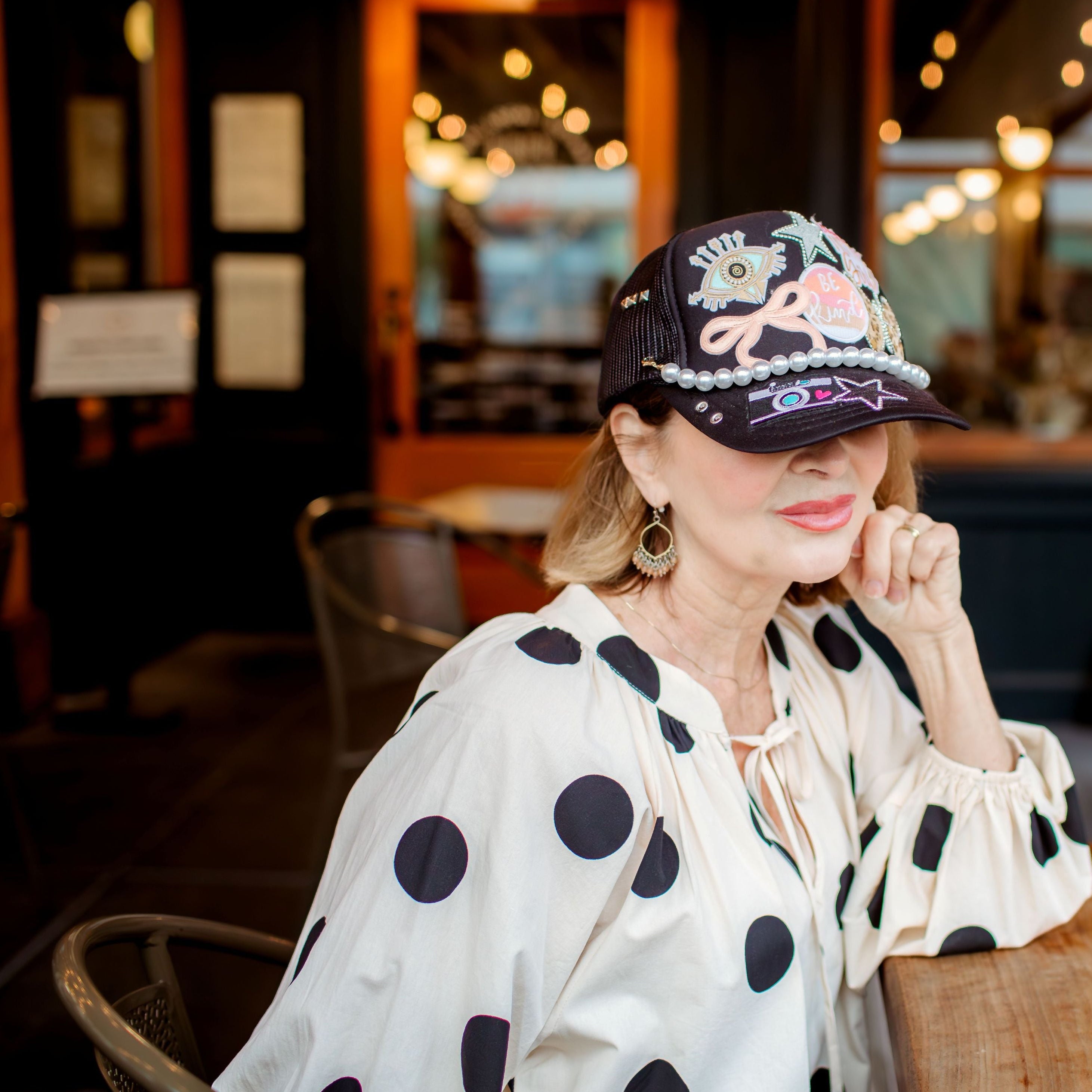 Woman wearing a polka dot blouse and cap sitting at a table in a restaurant.