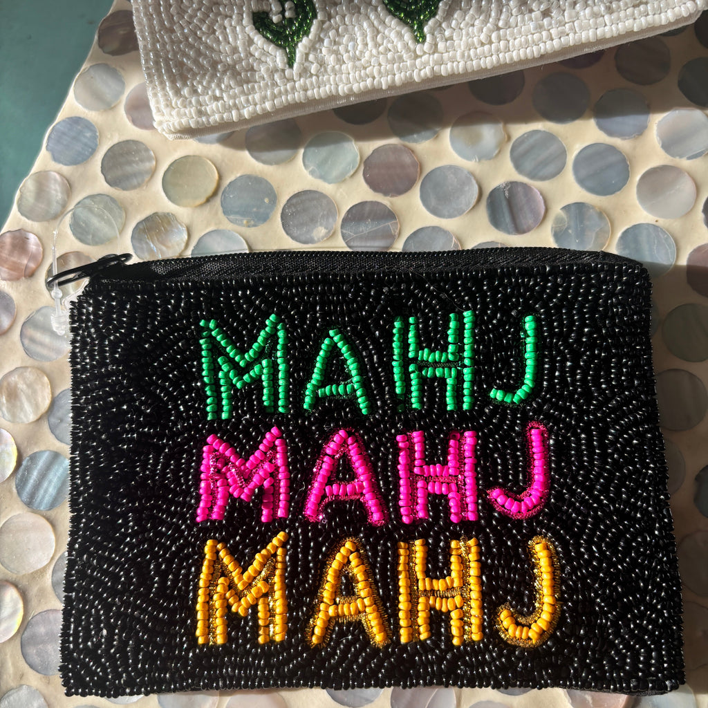 A black beaded zip pouch with the word 'MAHJ' repeated in green, pink, and yellow beads, placed on a mother-of-pearl shell-patterned surface.