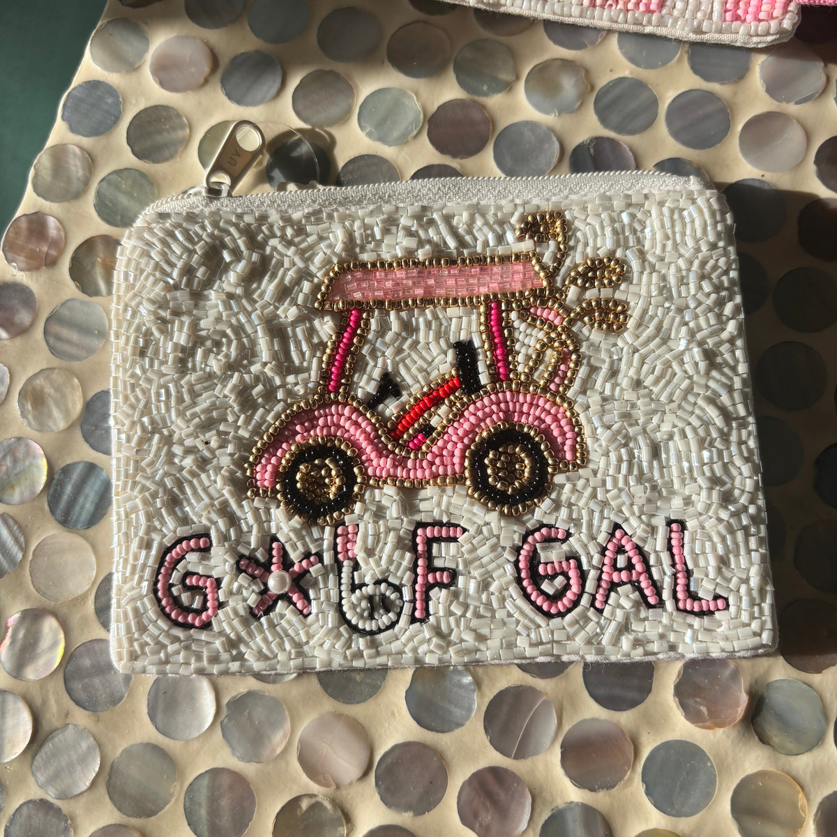 A white beaded zippered pouch featuring a pink and brown beaded golf cart and the words 'GOLF GAL' in pink and brown beads, displayed on a mother-of-pearl shell-patterned surface.