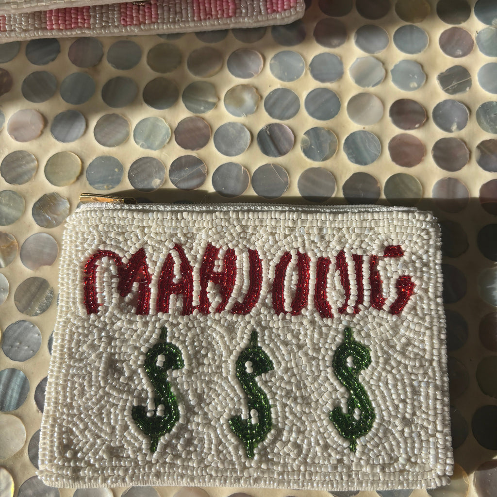 A close-up of a rectangular embroidered patch with the word "MAHONG" in red and three green dollar-sign symbols below it, placed on a circular-patterned surface.