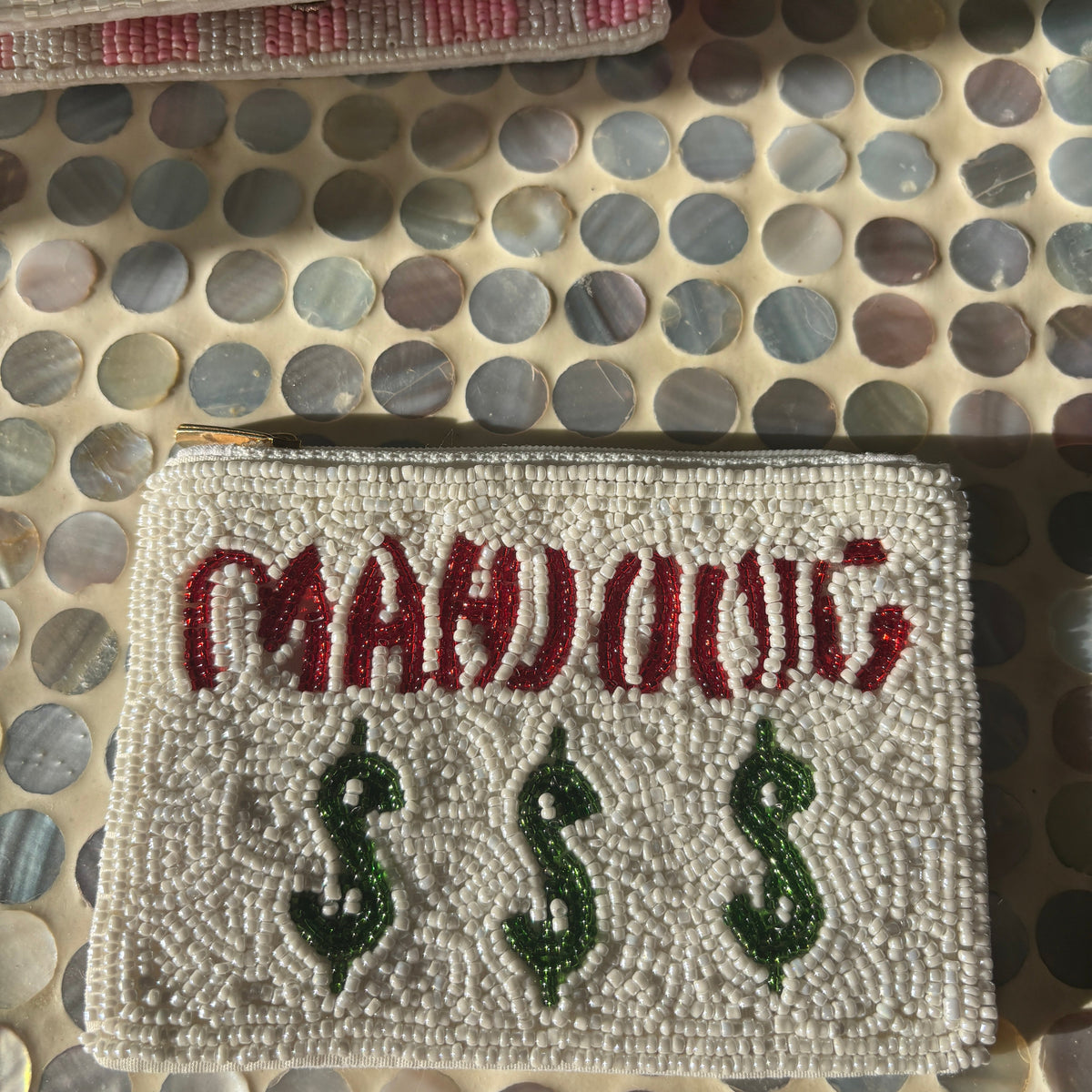 A close-up of a rectangular embroidered patch with the word "MAHONG" in red and three green dollar-sign symbols below it, placed on a circular-patterned surface.