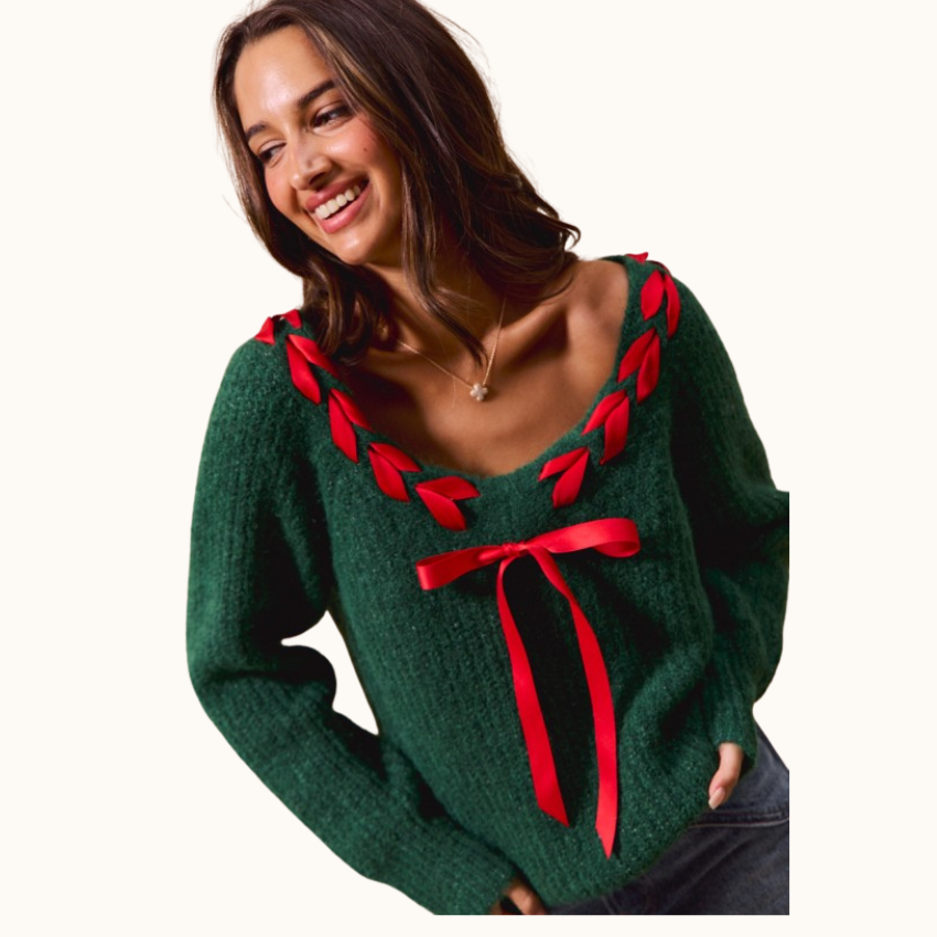 A woman wearing a dark green knit sweater with red ribbon trim along the scoop neckline and a large red ribbon bow at the center front, shown against a plain off-white background.