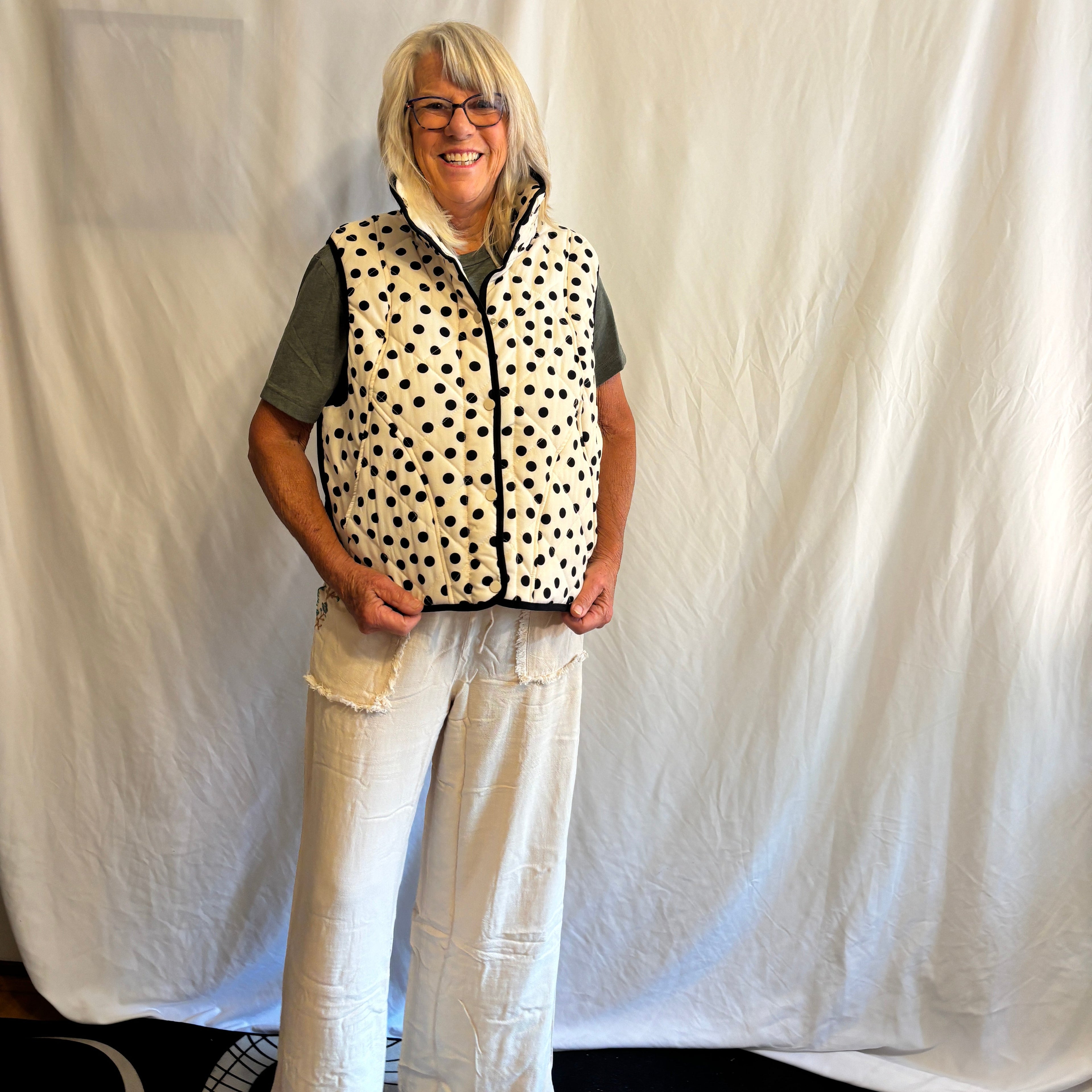 Person wearing a polka dot vest and white pants lying on a bed.