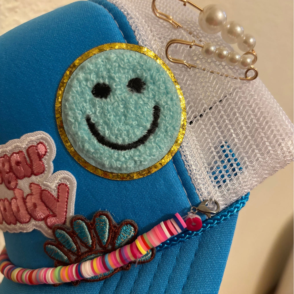 Blue pouch with smiley face patch, colorful bracelet, and pearl earrings on a beige background