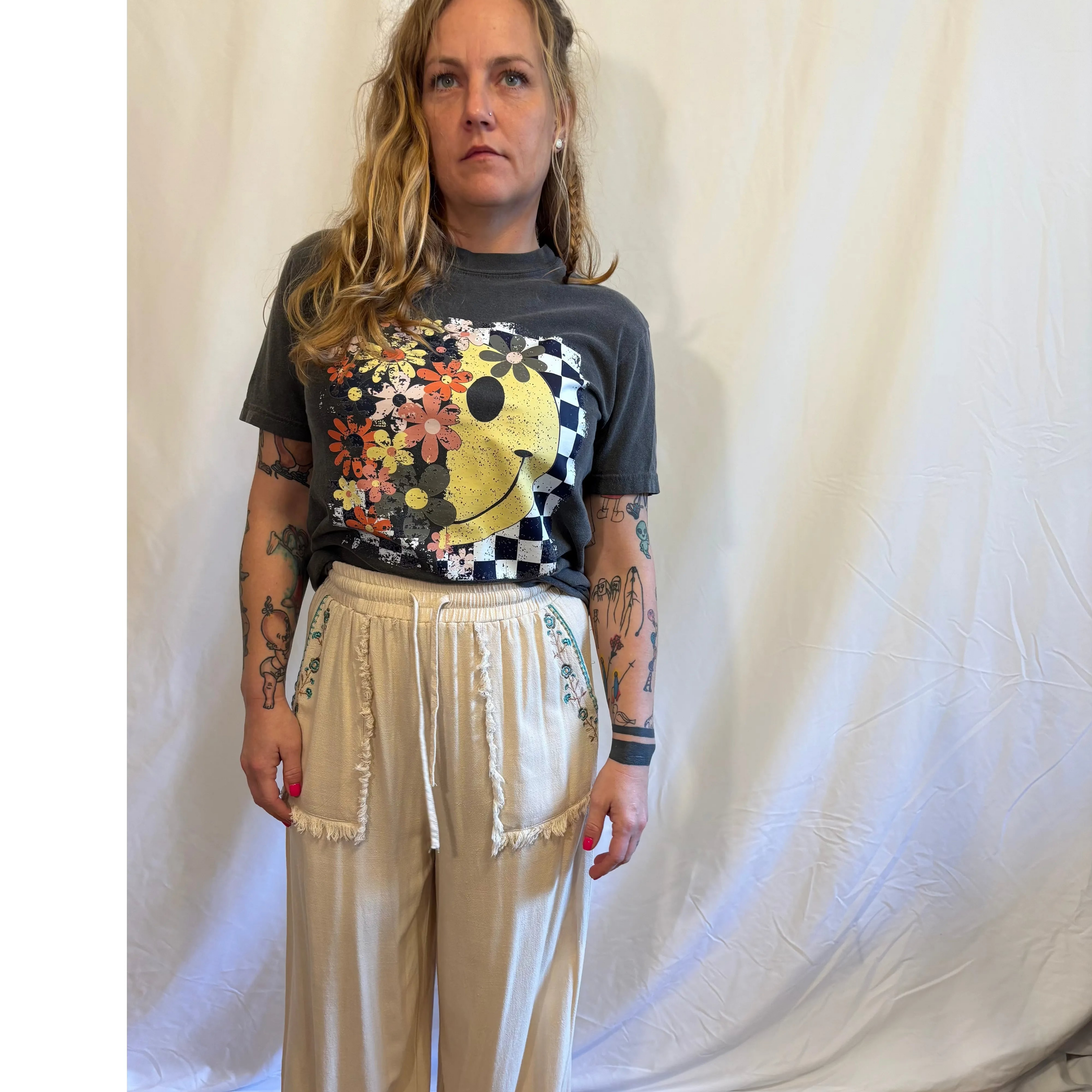 Person wearing a graphic t-shirt and beige pants against a white curtain background