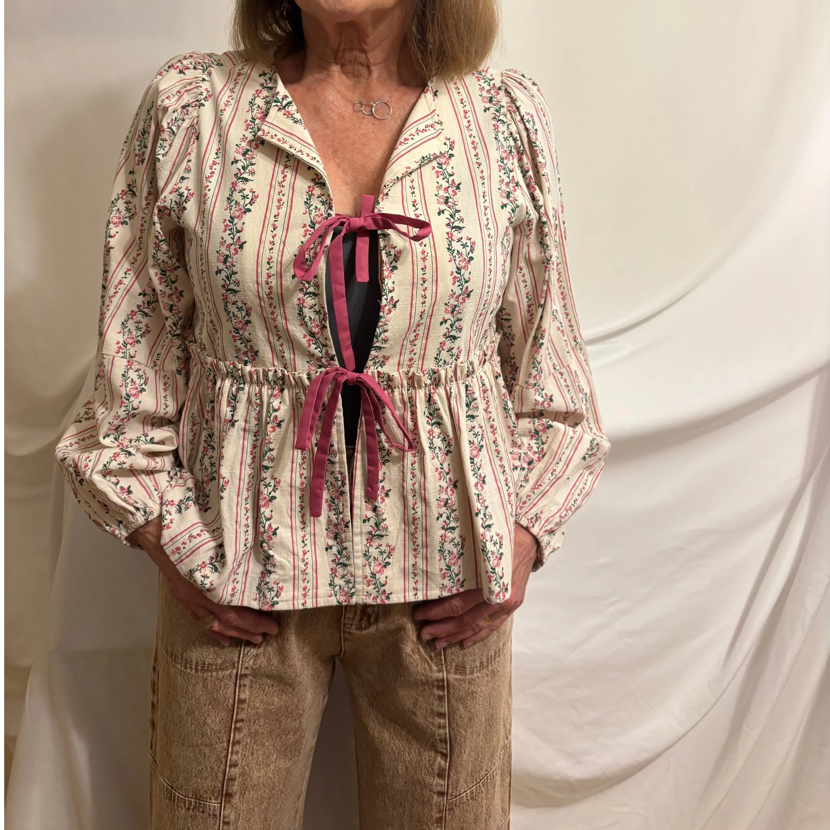 Woman wearing a patterned blouse with a pink ribbon against a white background
