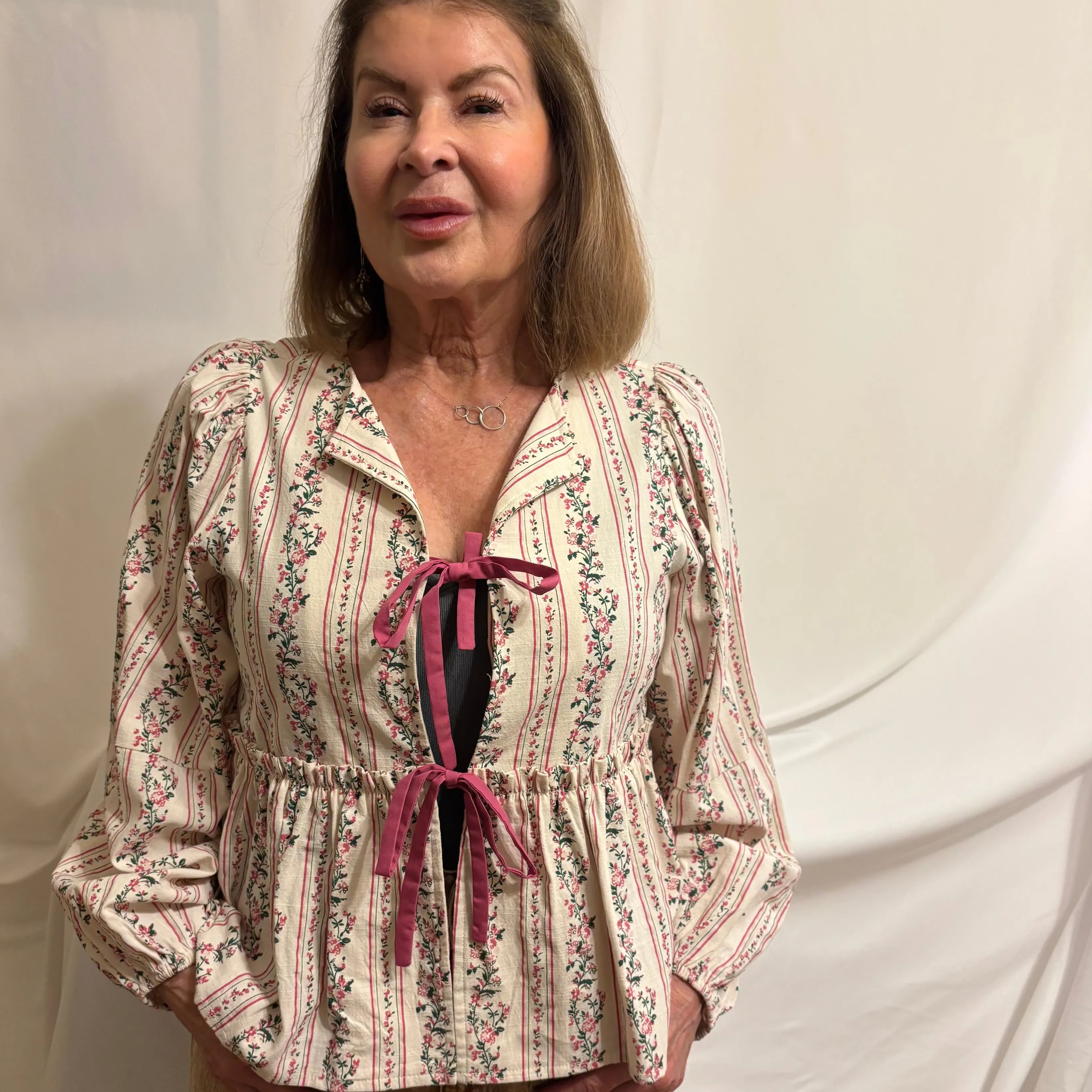 Woman wearing a patterned blouse with a pink ribbon against a white background