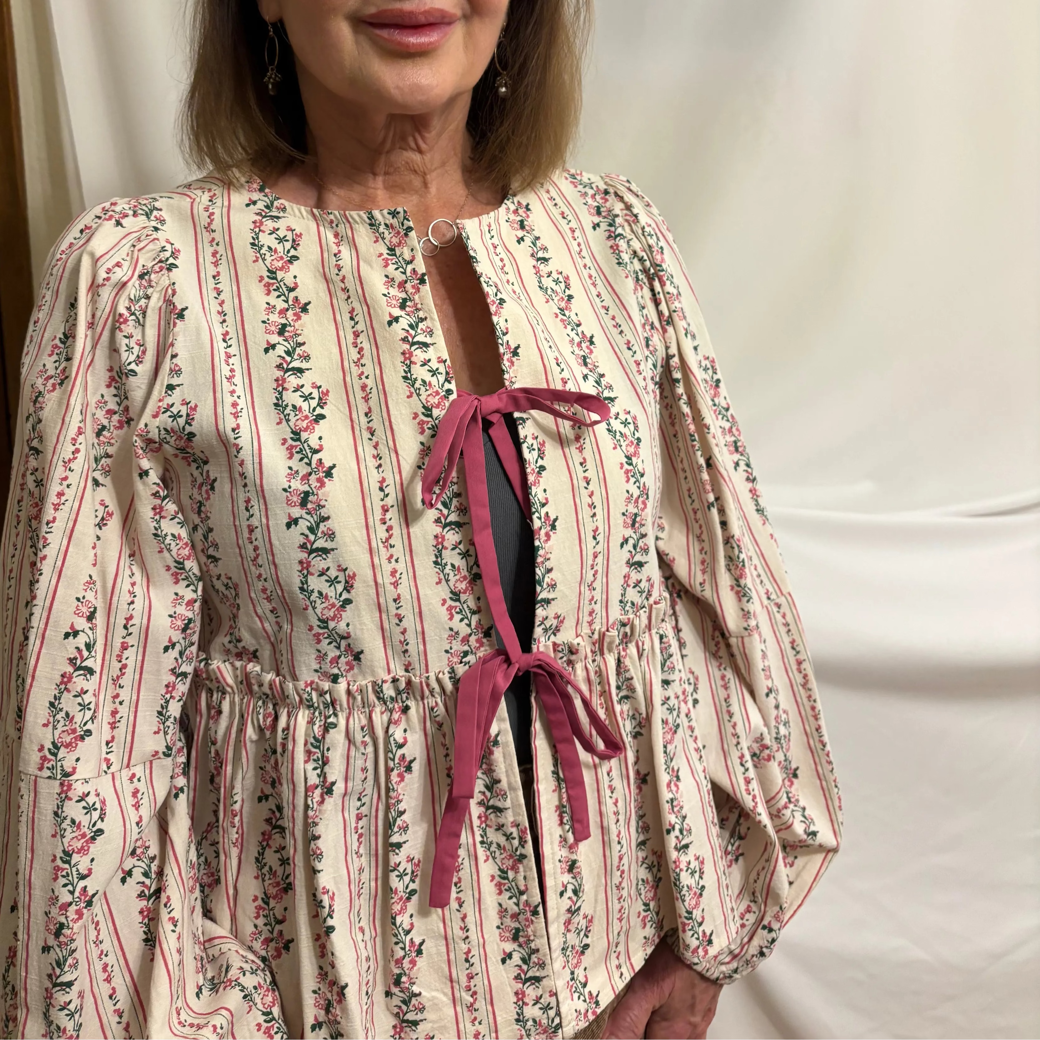 Woman wearing a floral dress with a pink bow against a plain background