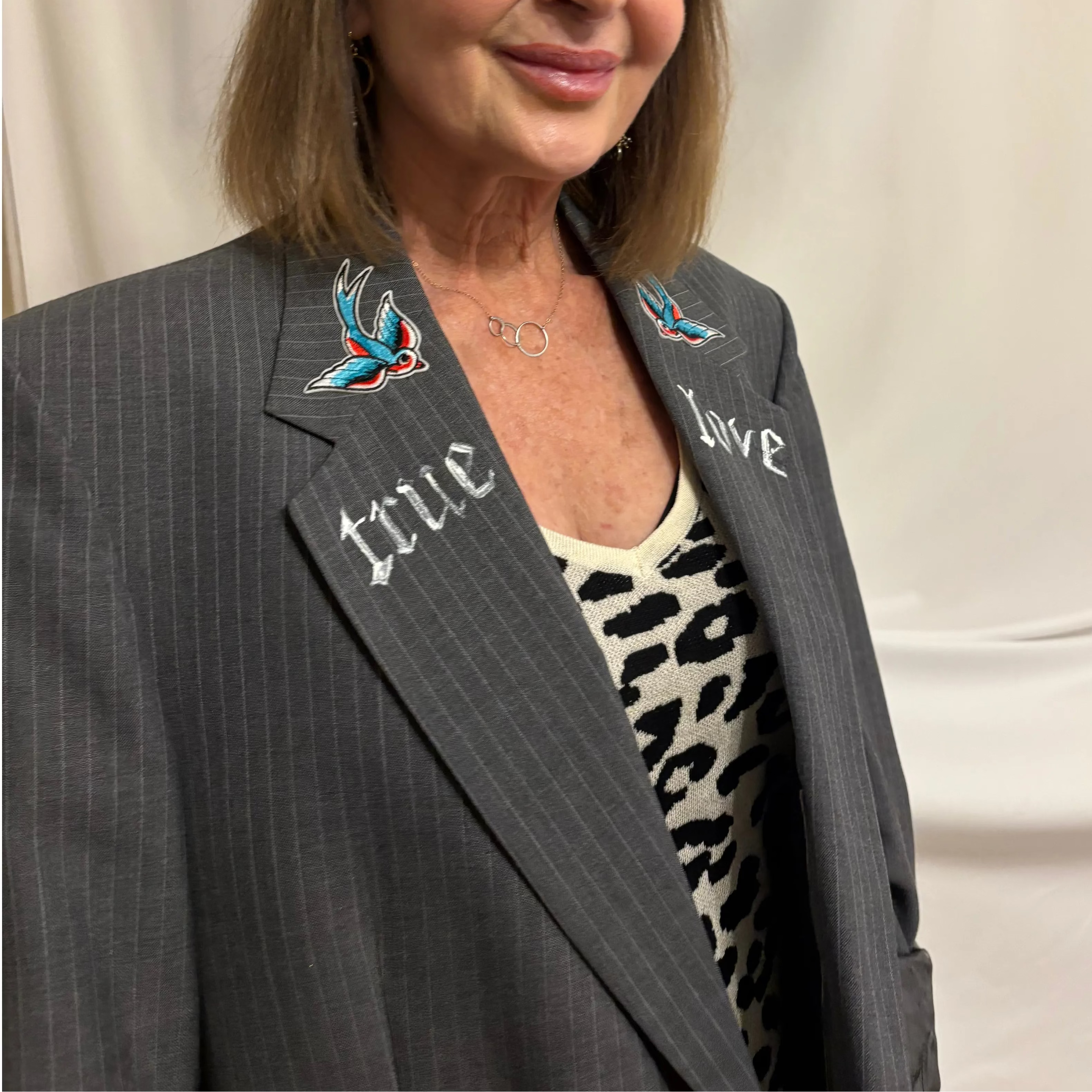 Woman wearing a gray blazer with embroidered text and designs on a plain background