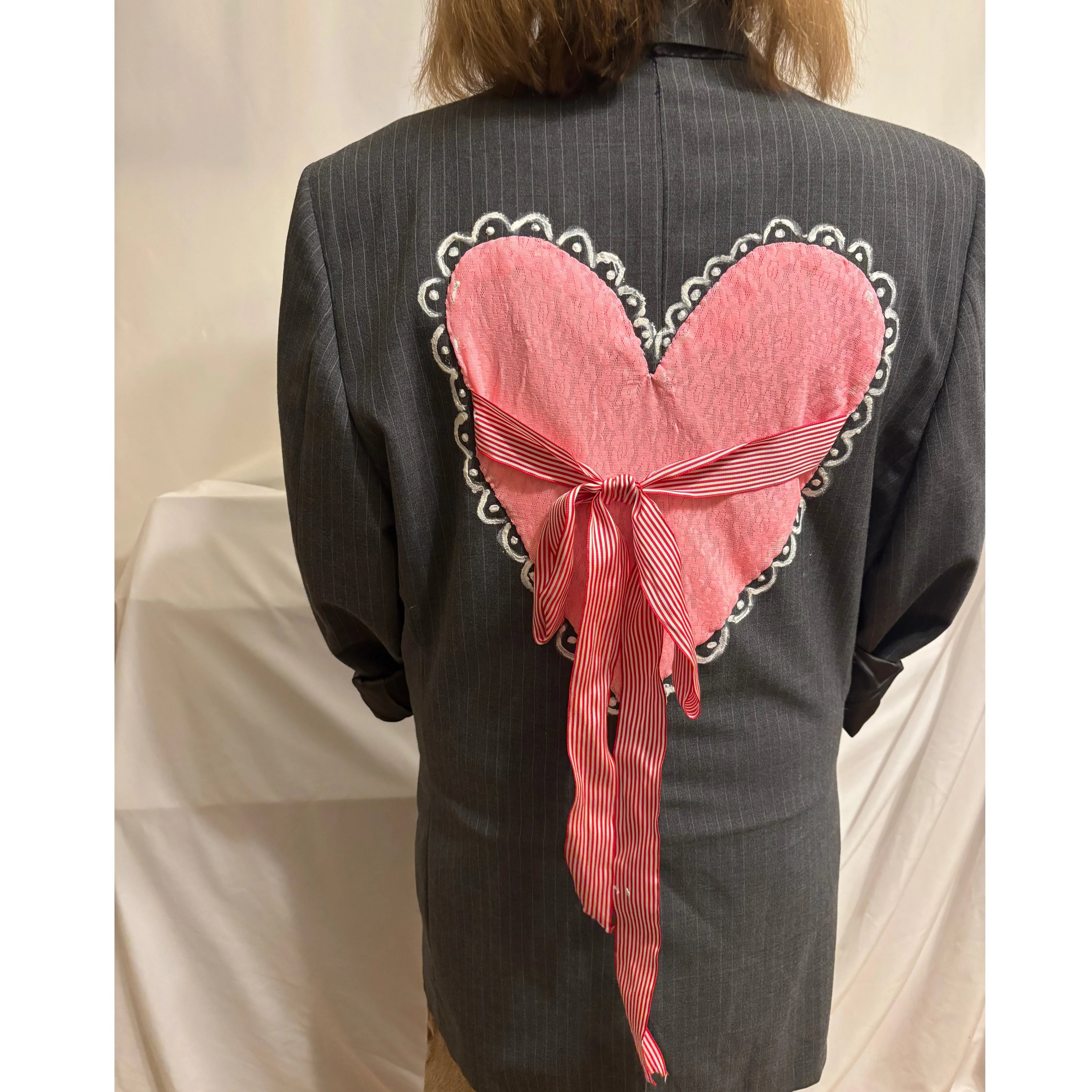 Person wearing a dark pinstripe suit with a pink heart-shaped bow on the back against a plain background