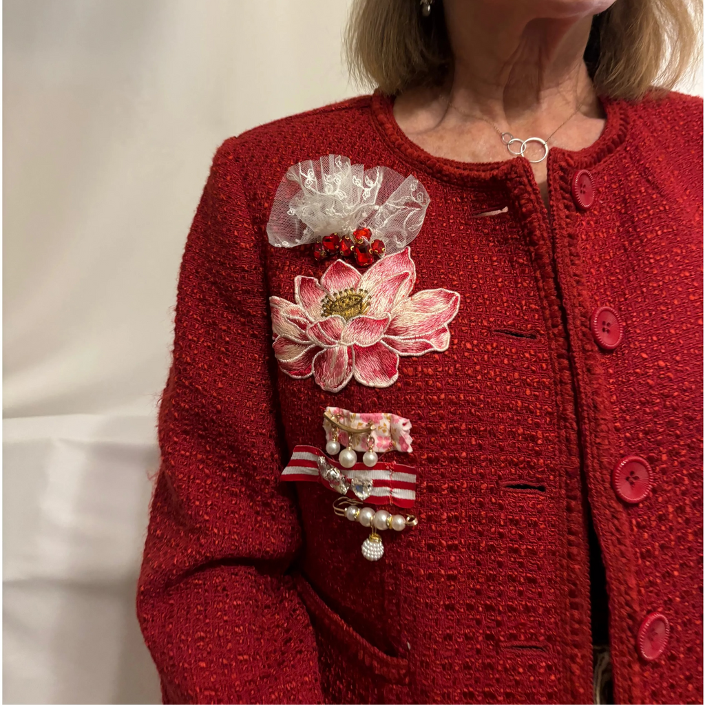 Woman wearing a red jacket with decorative brooches against a plain background