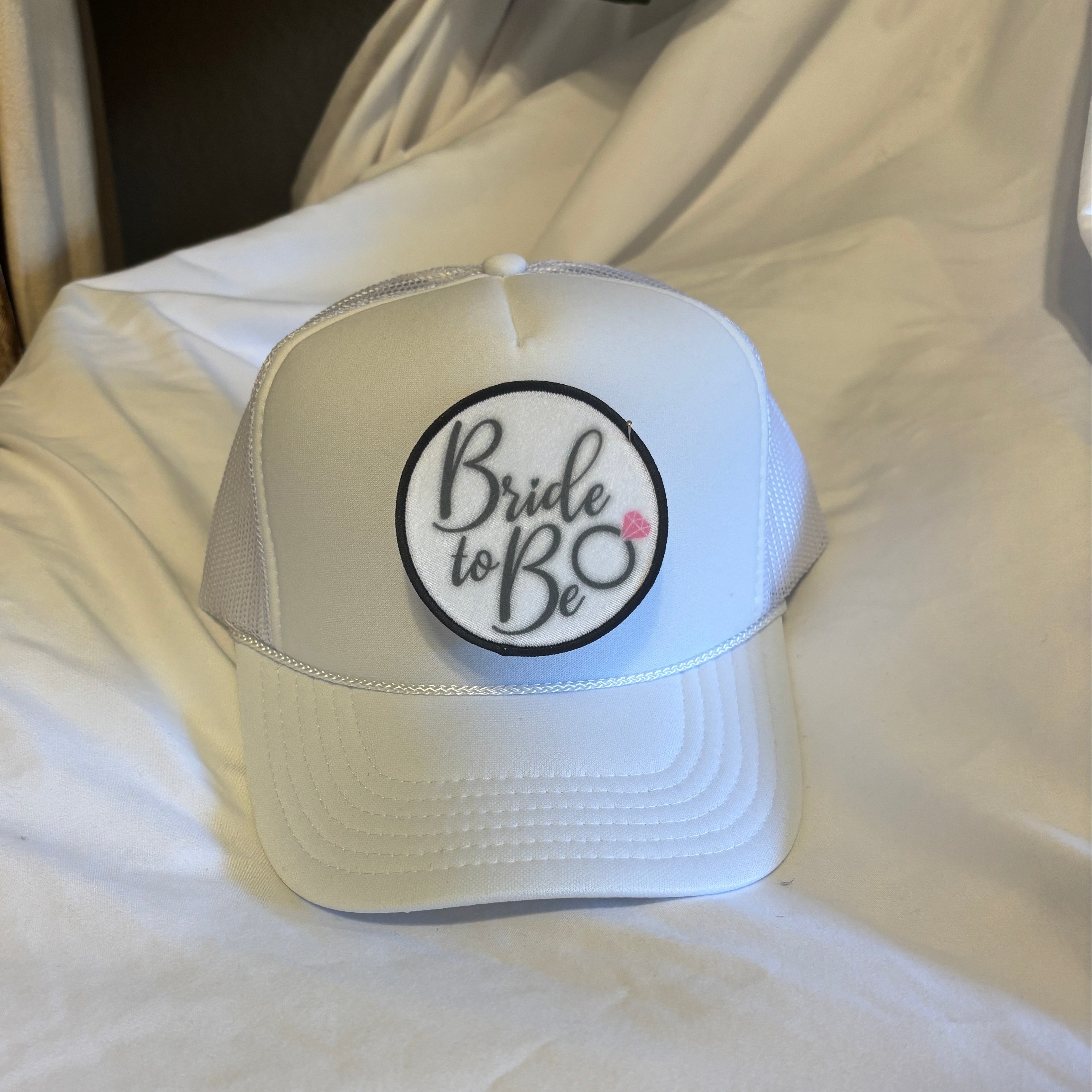 White cap with 'Bride to Be' text on a white surface