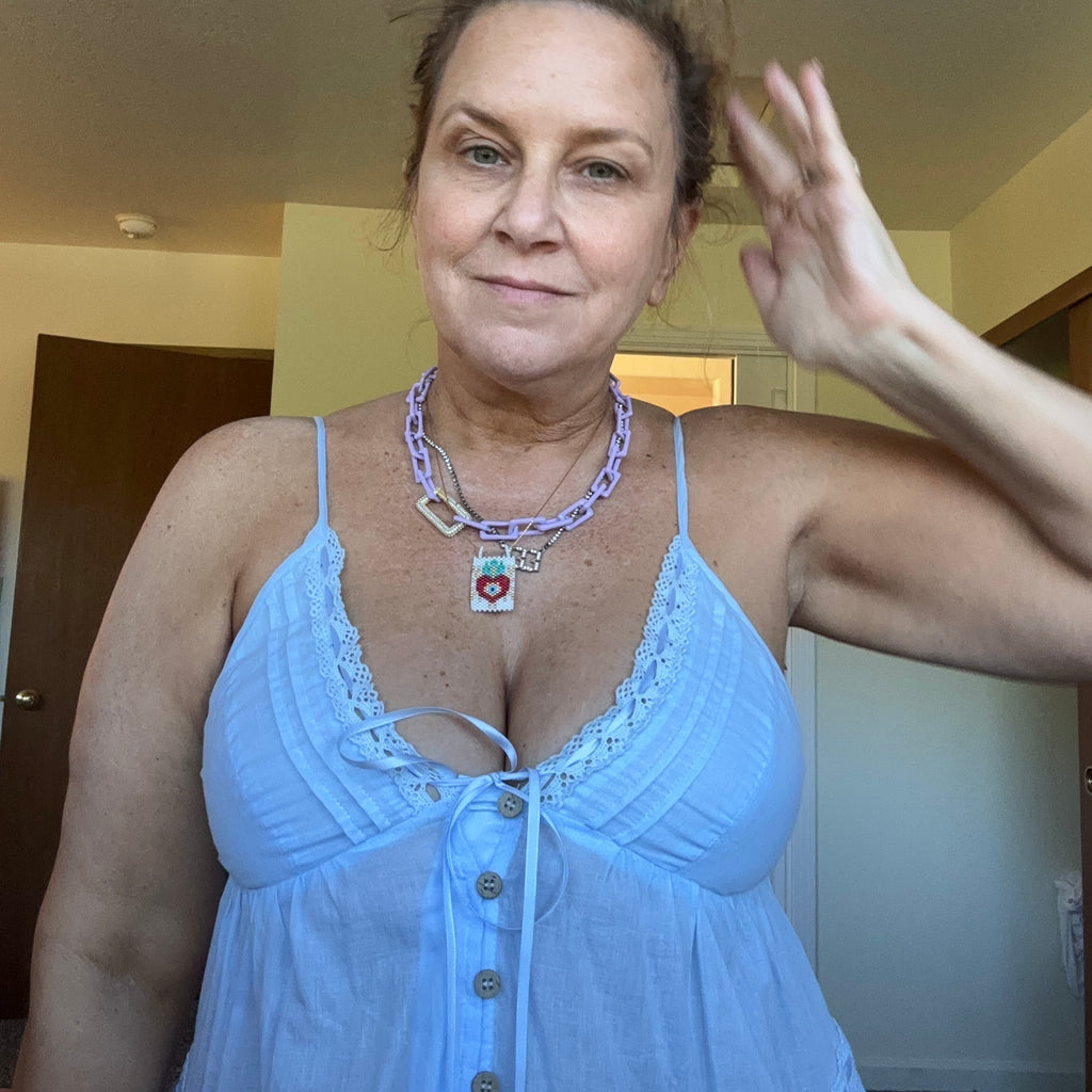 A woman wearing a light blue camisole top with lace trim and a button front, photographed indoors in a mirror-style selfie.