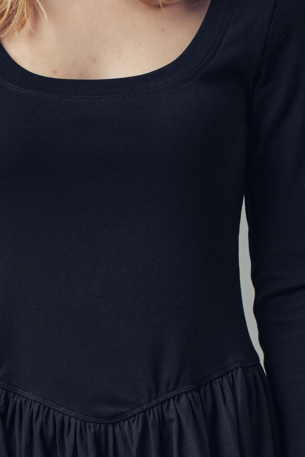 Close-up of a person wearing a black long-sleeve dress against a neutral background