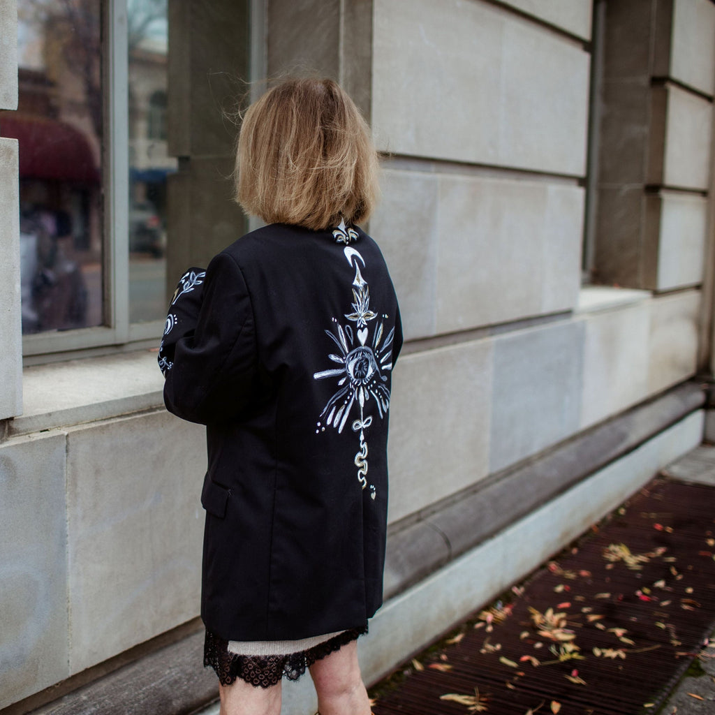 Person wearing a black jacket with white designs standing in front of a building.