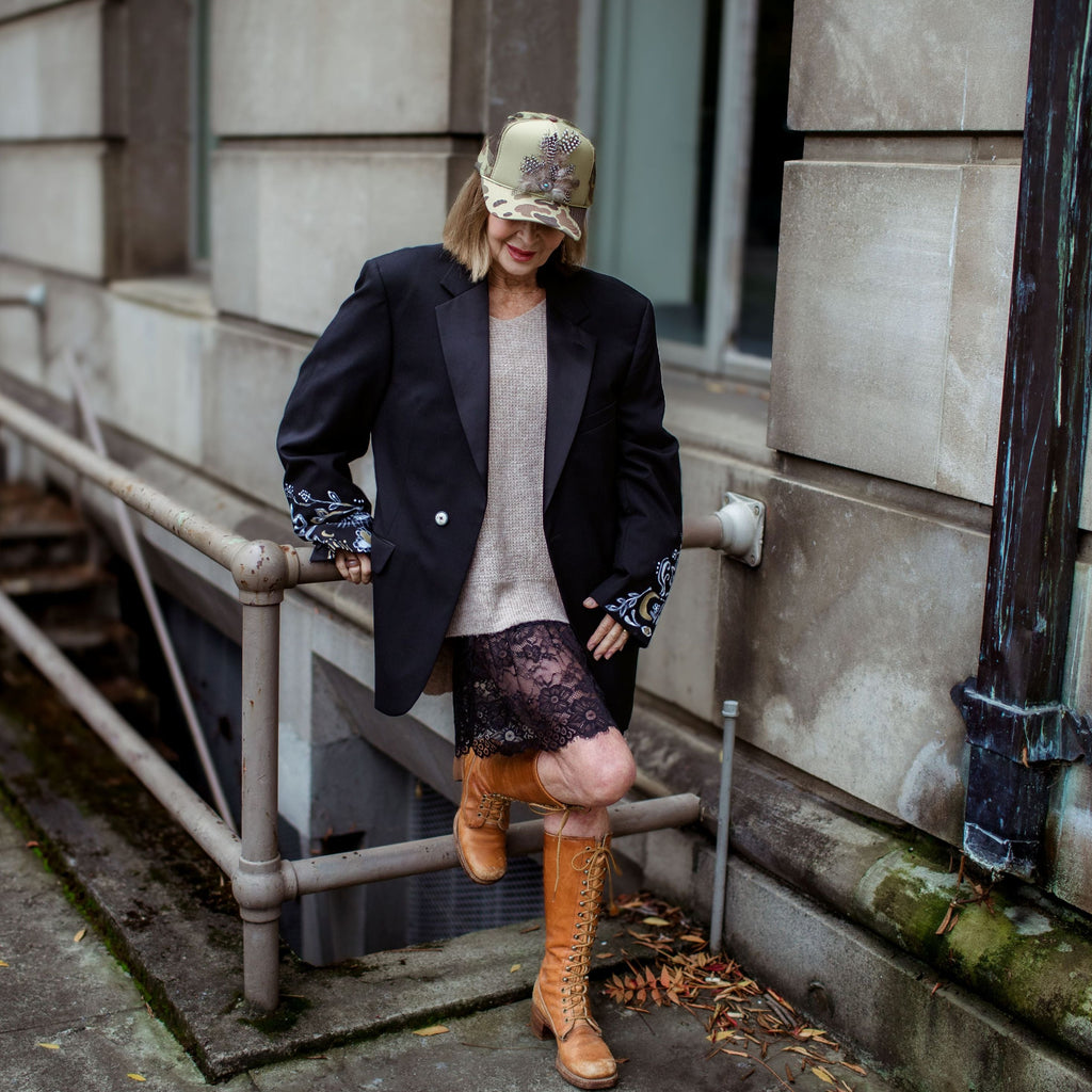 Person wearing a black coat and orange boots standing against a building wall.
