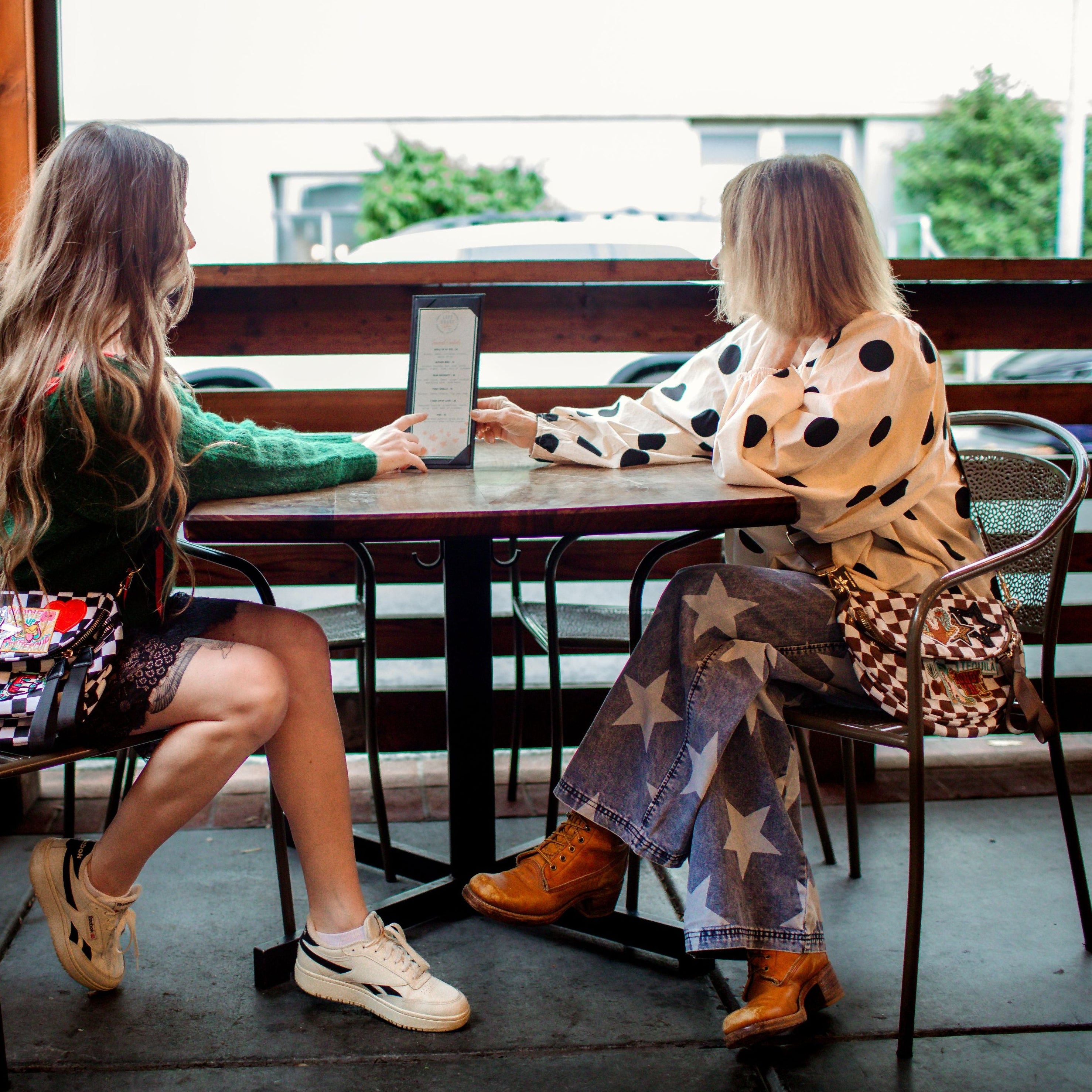 Two women sitting at a table on a balcony, using a tablet device.