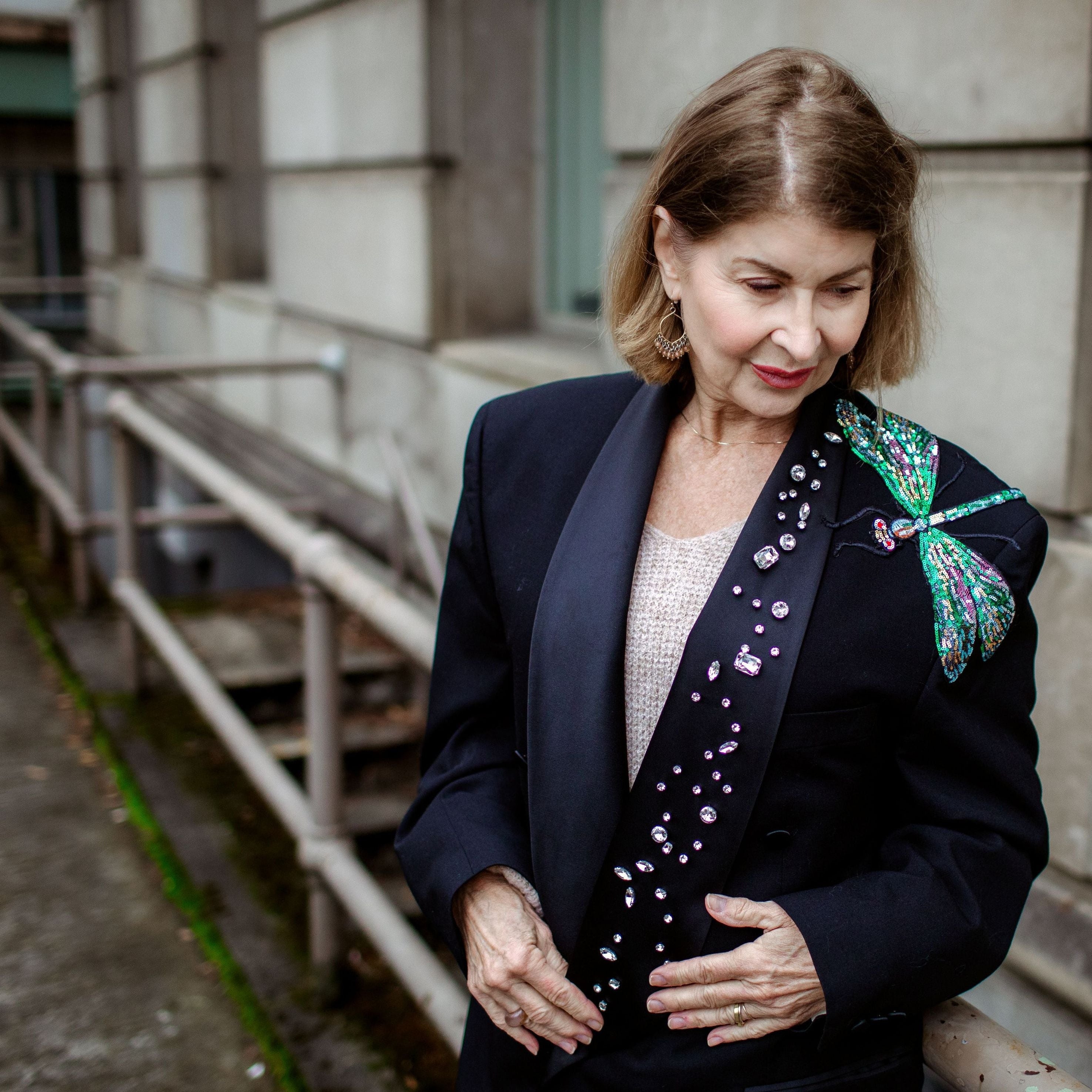 Woman in a dark blazer with floral details standing on a sidewalk.