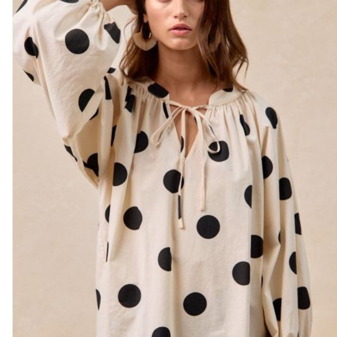 Woman wearing a polka dot blouse with long sleeves and a beige background
