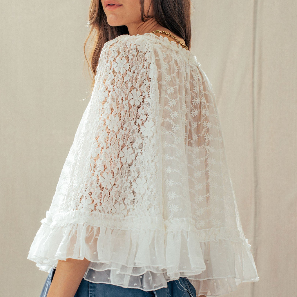 Woman wearing a white lace top over a blue outfit against a neutral background