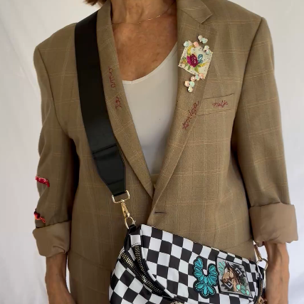 Woman wearing a brown blazer with floral embroidery and holding a checkered bag.